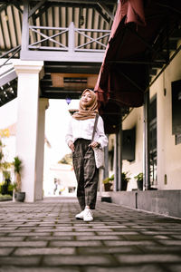 Portrait of woman on footpath against building