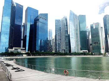 Modern buildings by river against sky in city