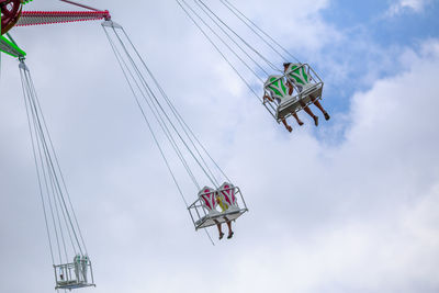 Low angle view of chain swing ride against cloudy sky