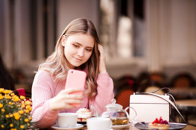 Smiling teenager girl taking selfie while sitting at cafe