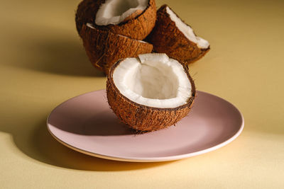 Coconut half in pink plate with nut fruits on cream yellow plain background