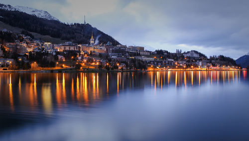 Illuminated city by river against sky