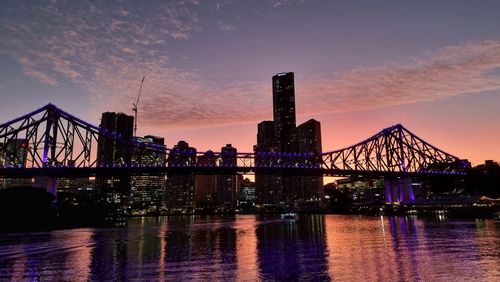 Illuminated bridge over river at sunset