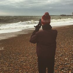 Rear view of woman photographing sea against sky