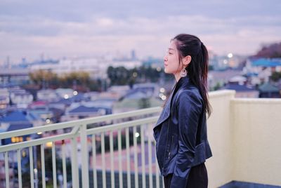 Side view of woman standing by railing while looking at cityscape