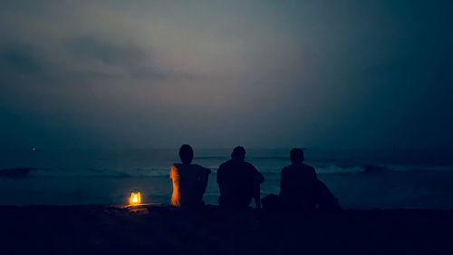 Rear view of people at beach against sky during sunset