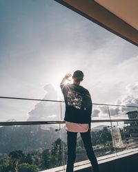 Rear view of man standing by railing against sky