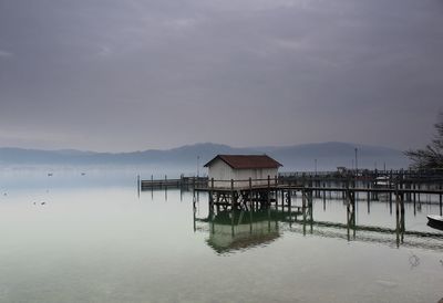 Stilt house on lake by building against sky