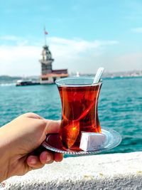 Midsection of person holding drink by sea against sky