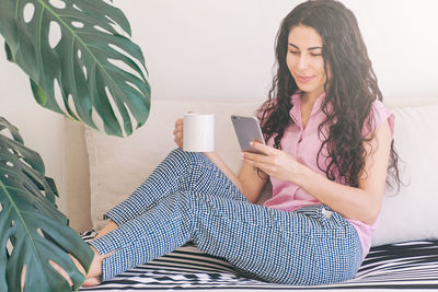 Young woman using mobile phone while sitting on sofa