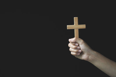 Close-up of hand holding cross against black background