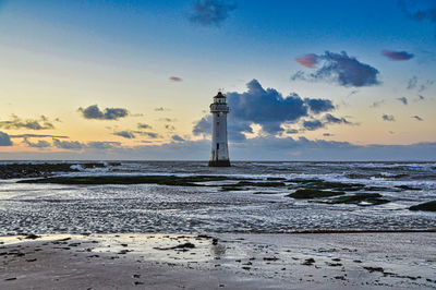 Lighthouse by sea against sky during sunset