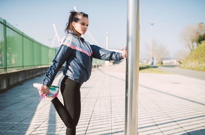 Young woman stretching on sidewalk against sky