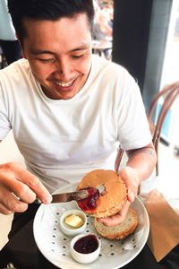 High angle view of smiling man applying jam on bread in cafe