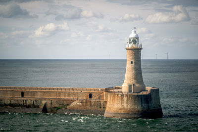 Lighthouse by sea against sky