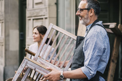 Colleagues holding wooden chairs while standing outside antique shop