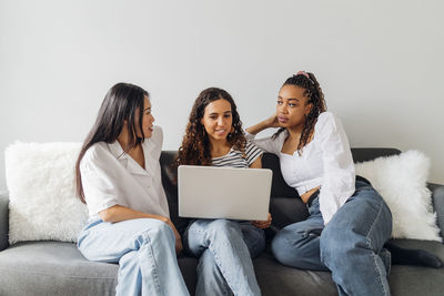 Young woman with laptop sitting amidst multiracial roommates in living room