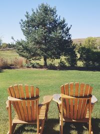 Chairs and table by trees on field against sky