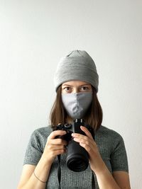 Young professional female photographer in reusable face mask holding camera pandemic times working