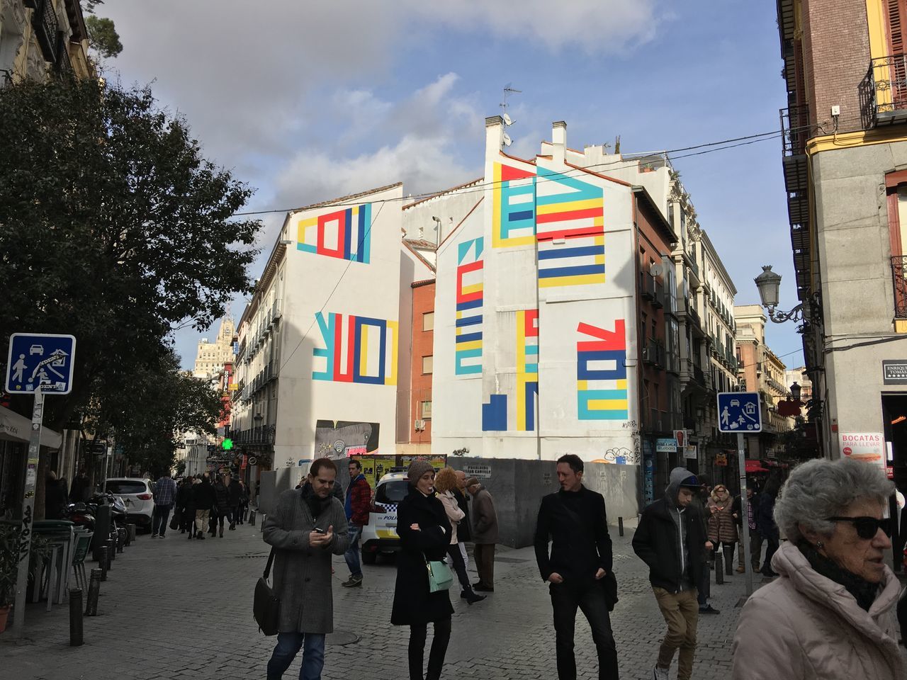 building exterior, architecture, built structure, street, men, large group of people, city, person, walking, city life, lifestyles, sky, city street, road, leisure activity, building, text, day, mixed age range