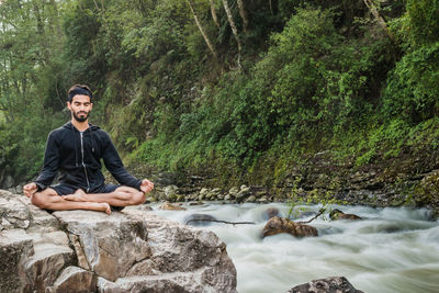 Full length of man practicing yoga on rock by stream