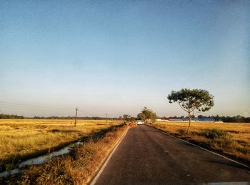 Road amidst field against clear sky