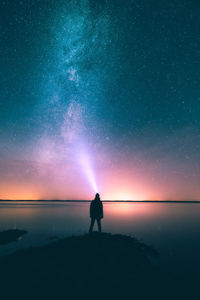 Silhouette person standing by lake against star field