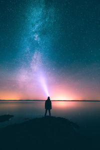 Silhouette woman standing by sea against sky at night