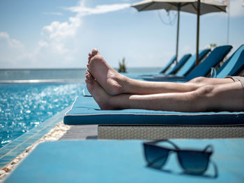 Low section of man relaxing on lounge chair in swimming pool