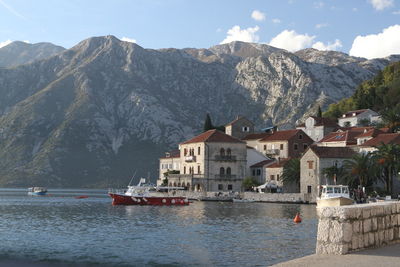 Sailboats in lake by buildings against mountains