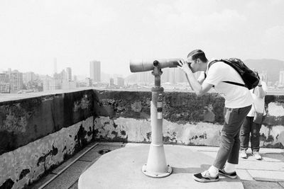 Side view of man standing against sky in city with binoculars