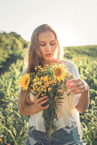 Beautiful young woman holding yellow flower in field