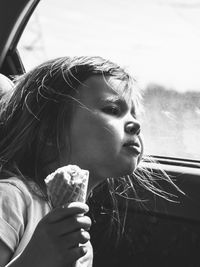 Girl holding ice cream cone while looking away in car