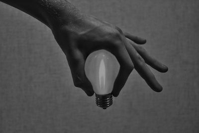 Close-up of hand holding light bulb against wall