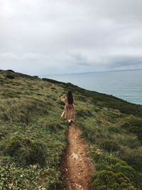 Rear view of woman walking on mountain against cloudy sky