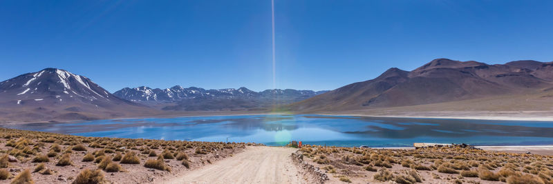 Panoramic view of road leading towards mountains against clear blue sky