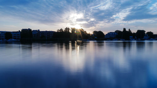 Silhouette buildings by lake against sky during sunset