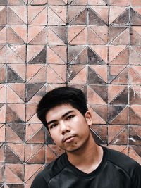 Portrait of young man standing against brick wall