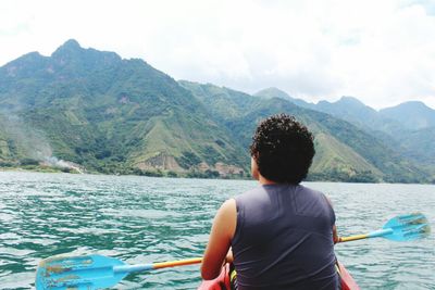 Rear view of man kayaking on lake by green mountains