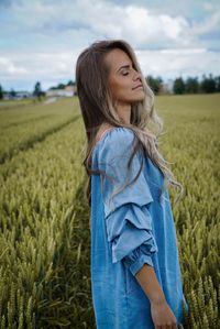 Side view of young woman with eyes closed standing on field against cloudy sky