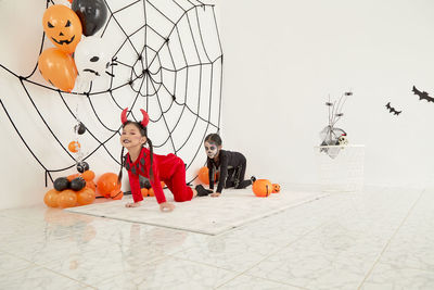 Full frame shot of boy with pumpkin on floor against orange wall during halloween