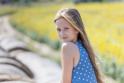 Portrait of pretty girl with long hair on top of the round hay bale smiling to the camera in summer