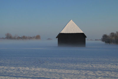 House by lake against clear sky during winter