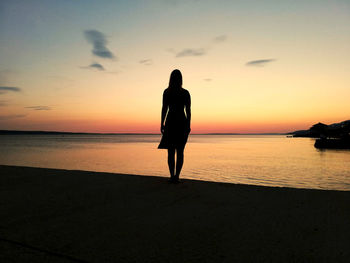 Silhouette woman standing on beach against sky during sunset