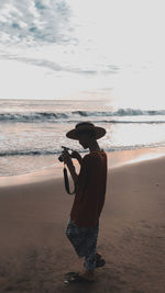 Rear view of man photographing at beach against sky