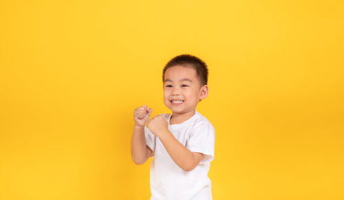 Portrait of smiling boy standing against yellow background