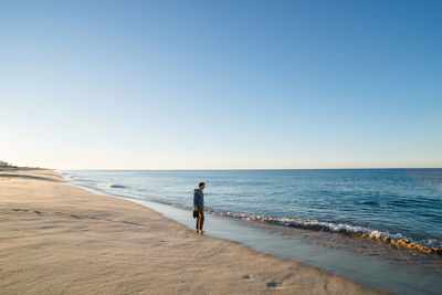 Man walking on beach against clear blue sky