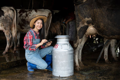 Portrait of woman using digital tablet by cows in shed