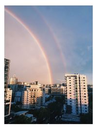 Rainbow over buildings in city against sky