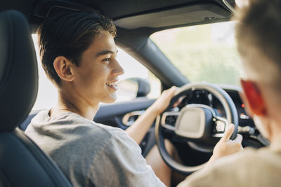 Over the shoulder view of happy son learning to drive with father in car